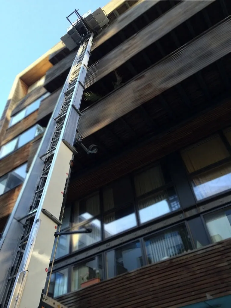 Uitgeschoven ladderlift langs de gevel van een appartementsgebouw, van onderaf gezien